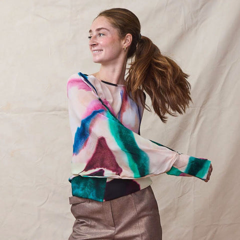 Woman wears a long sleeve silk top in watercolor print with belted metallic trousers