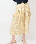Beige midi skirt with delicate floral embroidery and soft pleats, worn with a navy cardigan.