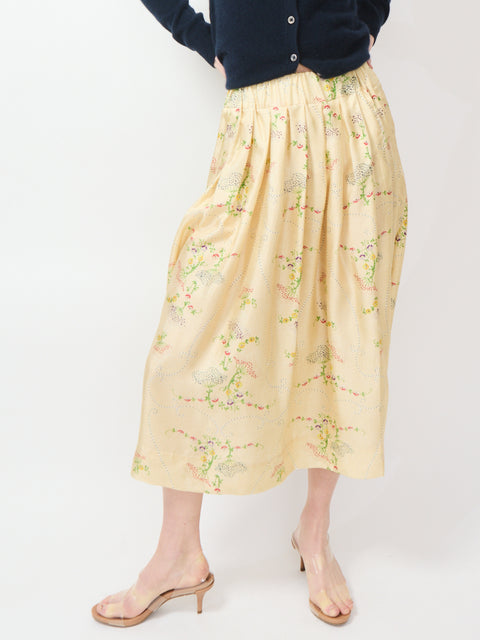 Beige midi skirt with delicate floral embroidery and soft pleats, worn with a navy cardigan.