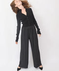 Woman wearing a black cardigan and pleated black pants on a white background