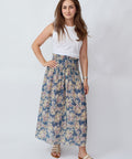 Woman wearing a white top and floral skirt on a plain background