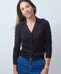 Woman wearing a black ribbed sweater and blue jeans against a light gray background