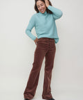 Dark chocolate velvet pants with a straight leg fit worn with a light blue turtleneck sweater.