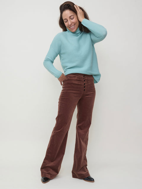 Dark chocolate velvet pants with a straight leg fit worn with a light blue turtleneck sweater.