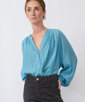 Woman wearing a light blue blouse with balloon sleeves against a white background