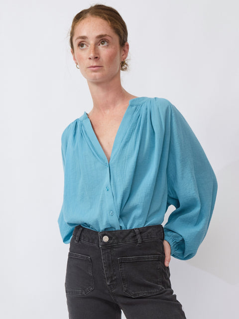 Woman wearing a light blue blouse with balloon sleeves against a white background