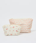 Two floral-patterned makeup pouches in soft ecru tones, one smaller with delicate rose prints, one larger with subtle peach.