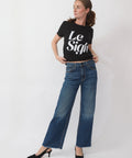 Woman wearing a black t-shirt with 'Le Sigh' text and blue jeans on a white background