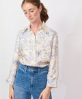 Woman wearing a floral blouse and blue jeans against a white background