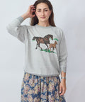 Woman wearing a gray sweatshirt with horse design on a plain background