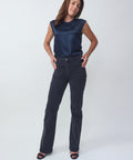 Woman wearing a navy sleeveless top and dark jeans on a white background