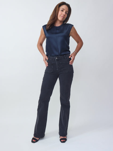 Woman wearing a navy sleeveless top and dark jeans on a white background