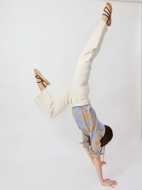 Off-white denim jeans with a straight-leg fit worn by a person doing a handstand, paired with strappy brown sandals.