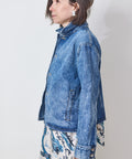 Woman wearing a blue denim jacket over a patterned dress on a plain background