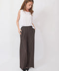 Woman wearing a white sleeveless top and brown pleated pants on a white background