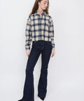 Woman wearing indigo flared jeans paired with beige and navy plaid button-up shirt.