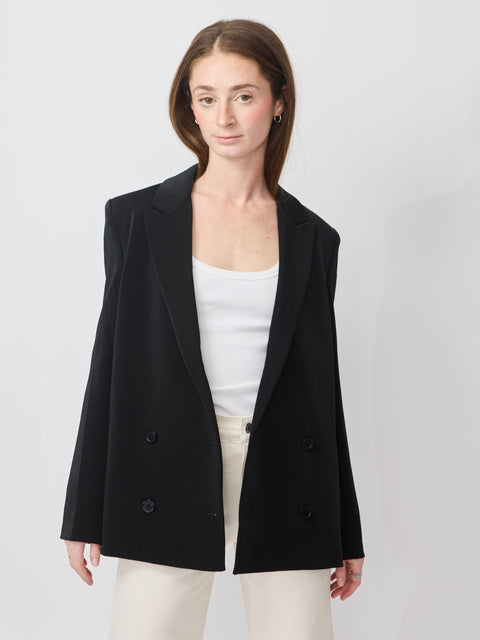 Black double-breasted blazer with structured shoulders and tailored fit worn over a white top.