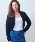 Woman wearing a navy cardigan, white top, and blue jeans against a light gray background