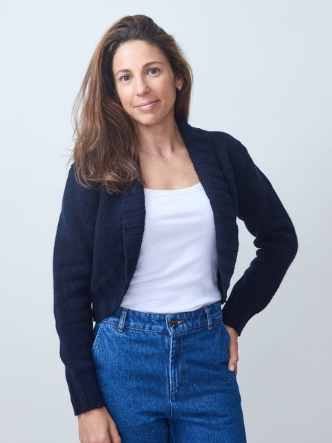 Woman wearing a navy cardigan, white top, and blue jeans against a light gray background
