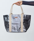 Person holding a metallic silver tote bag with beige handles against a light gray background