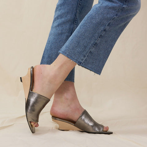 Pretty woman wears a pair of metallic leather slides with wooden demi-wedge heel