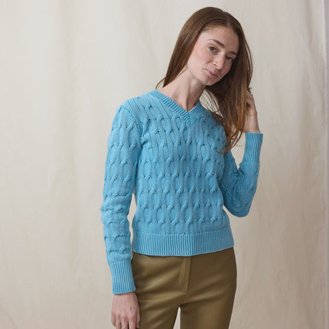 Young lady wears a cable knit blue sweater with brown leather pants