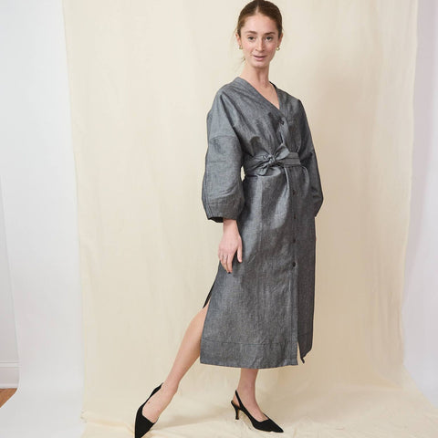 Beautiful young woman wears a v-neck, midi dress with matching belt and full button front, and a pair of black suede slingback shoes