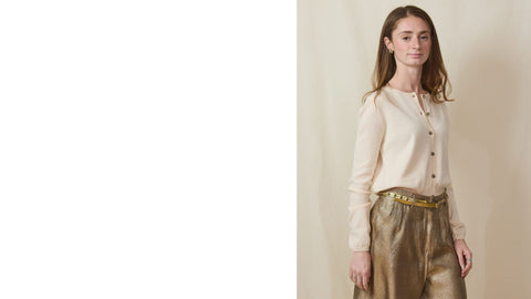 tall young woman wears a cream cotton/cashmere cardigan and gold bermuda shorts.