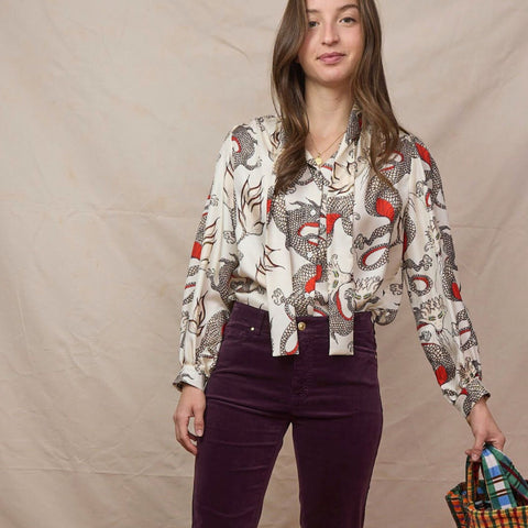 Young brunette wears a long sleeve silk top with a dragon print and dark plum corduroy high waisted pants