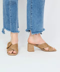 Beige suede open-toe sandals with block heels and knotted straps, worn with frayed hem jeans.