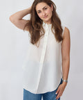 Woman wearing a white sleeveless blouse and blue jeans on a plain background