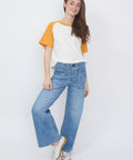 High-waist light blue denim jeans with wide leg and button fly worn with white and orange raglan t-shirt.