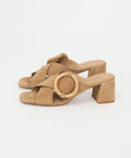 Beige suede sandals with block heels and round buckle detail on crisscross straps.