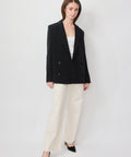 Black double-breasted blazer with structured shoulders and notch lapels, worn over white top.