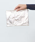 Hand holding a white textured pouch against a light gray background