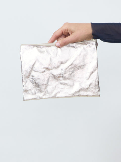 Hand holding a white textured pouch against a light gray background