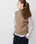 Sleeveless pecan cable-knit turtleneck sweater layered over white striped button-up shirt.