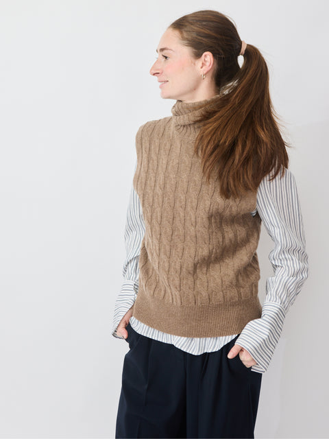 Sleeveless pecan cable-knit turtleneck sweater layered over white striped button-up shirt.