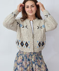 Woman wearing a patterned cardigan over a floral dress on a plain background