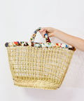 Woven basket with colorful handle held by a person on a white background