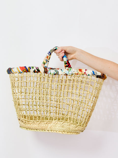 Woven basket with colorful handle held by a person on a white background