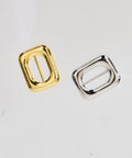 Two rectangular metal belt buckles, one gold and one silver, with rounded edges and central bar.