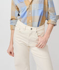 High-waist bone-colored denim jeans with front pockets and button fly worn with rolled-sleeve plaid shirt.