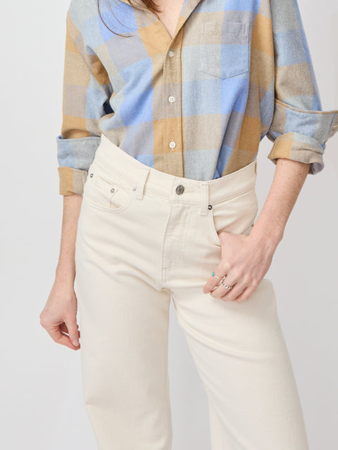 High-waist bone-colored denim jeans with front pockets and button fly worn with rolled-sleeve plaid shirt.