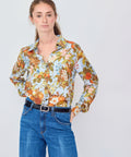 Woman wearing a floral blouse and blue jeans against a plain background