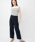 Navy high-waisted wide-leg pants with pleats worn with white sleeveless top and brown sandals.