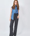 Woman wearing a blue patterned top and black pants on a white background