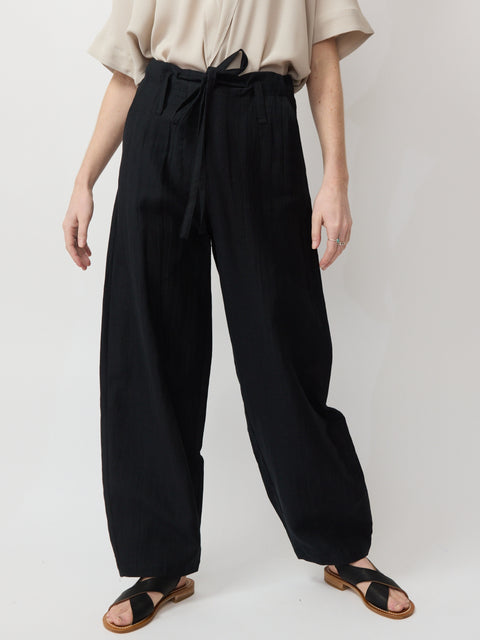 Black wide-leg pants with high waist and fabric belt, styled with beige top and black sandals.