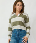 Woman wearing a green and white striped sweater with blue jeans on a plain background