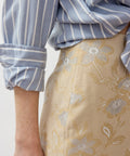 Beige pencil skirt with subtle floral embroidery paired with blue and white striped shirt.